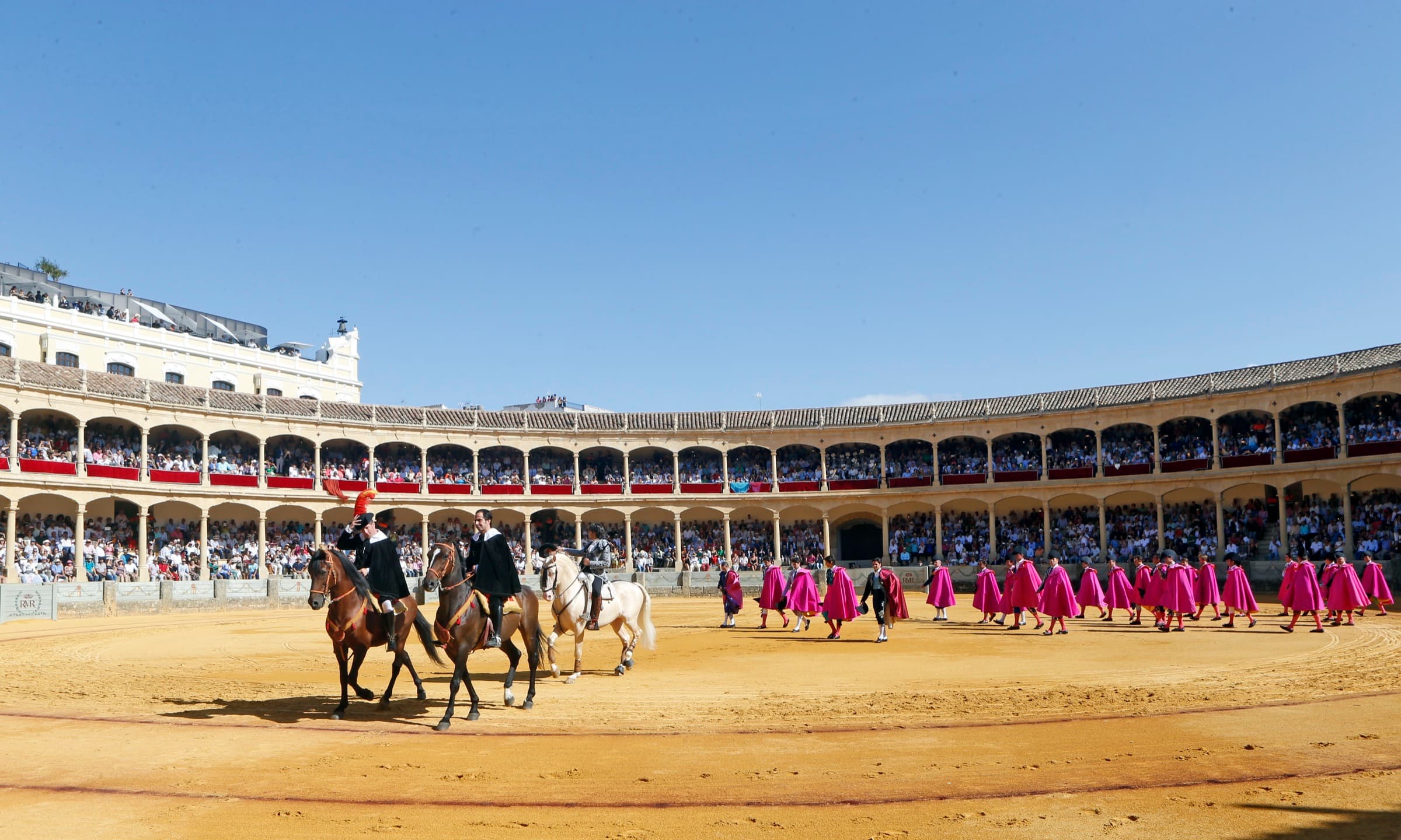 Paseíllo de la Corrida Goyesca de Ronda: los alguacilillos a caballo y las cuadrillas con capotes de paseo cruzan el albero bajo la doble galería llena de público